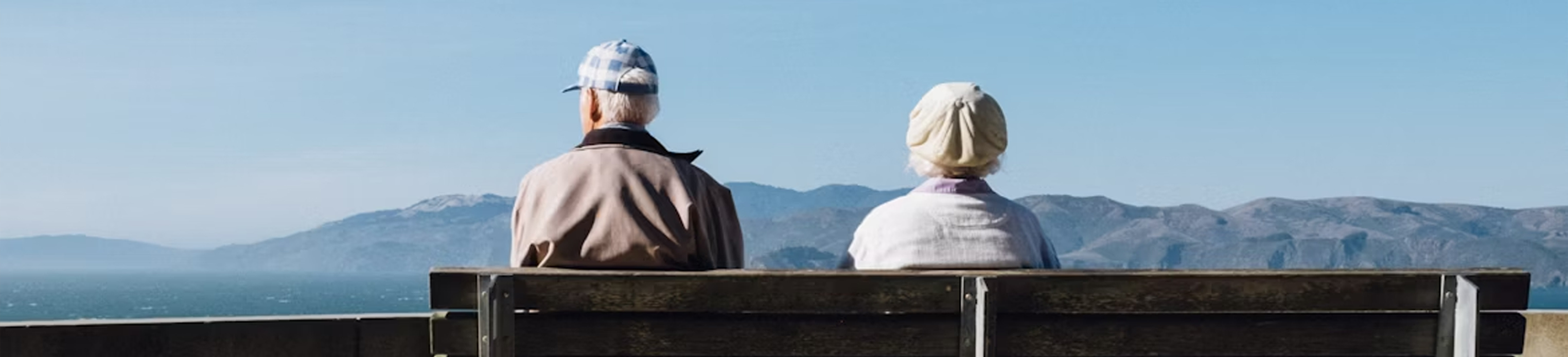 An elderly couple sitting on a bench by the ocean, gazing at the serene landscape.